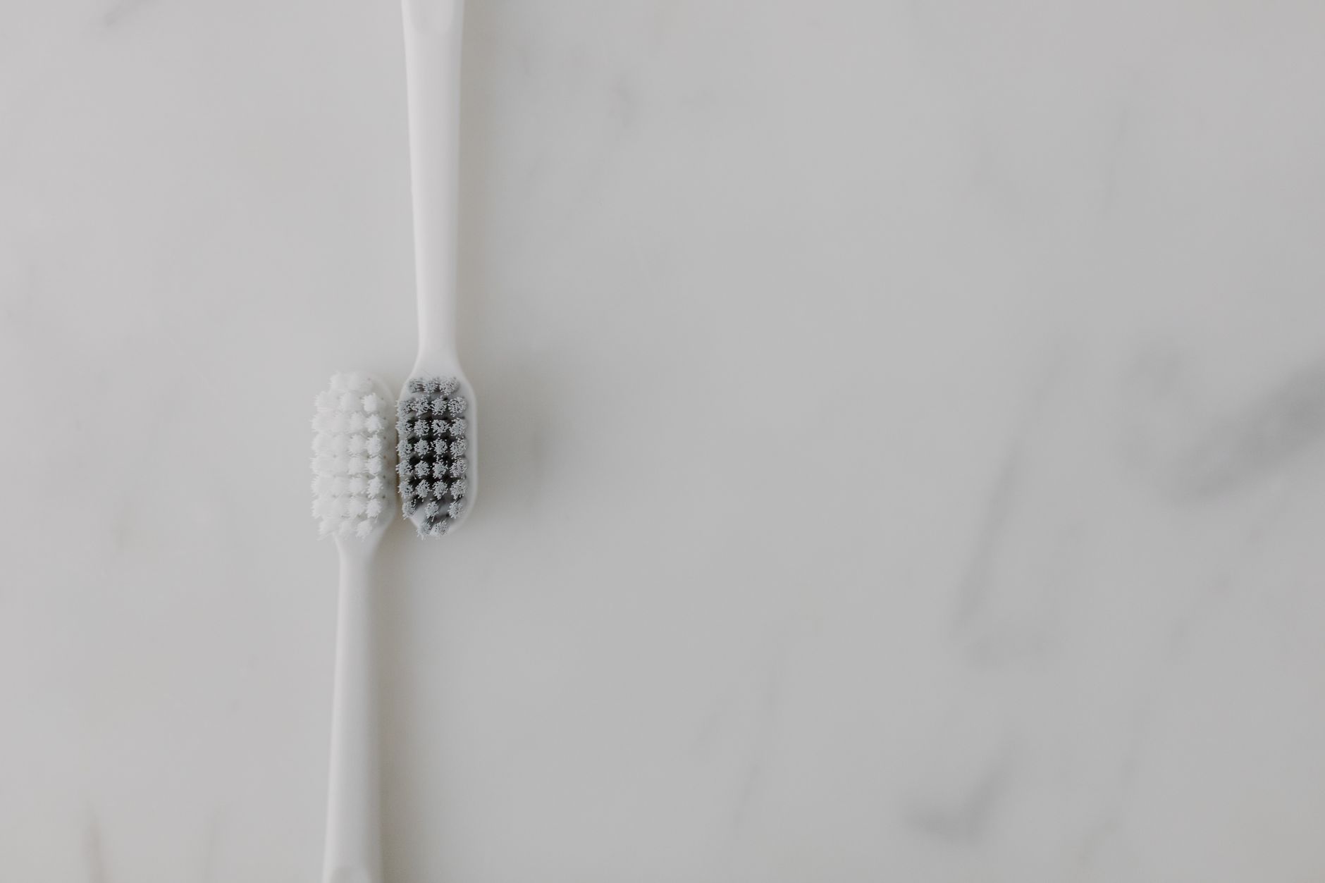 Two toothbrushes lying on a white marble surface