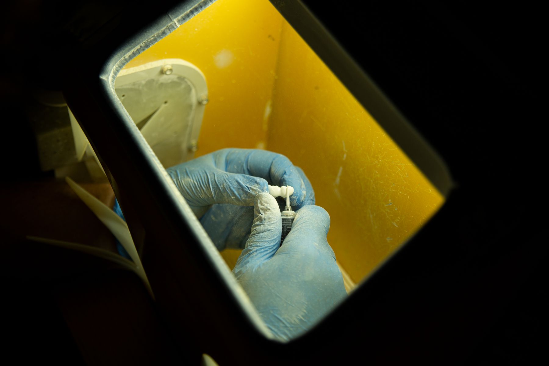 Dental technician in gloves shaping a ceramic dental crown in a laboratory