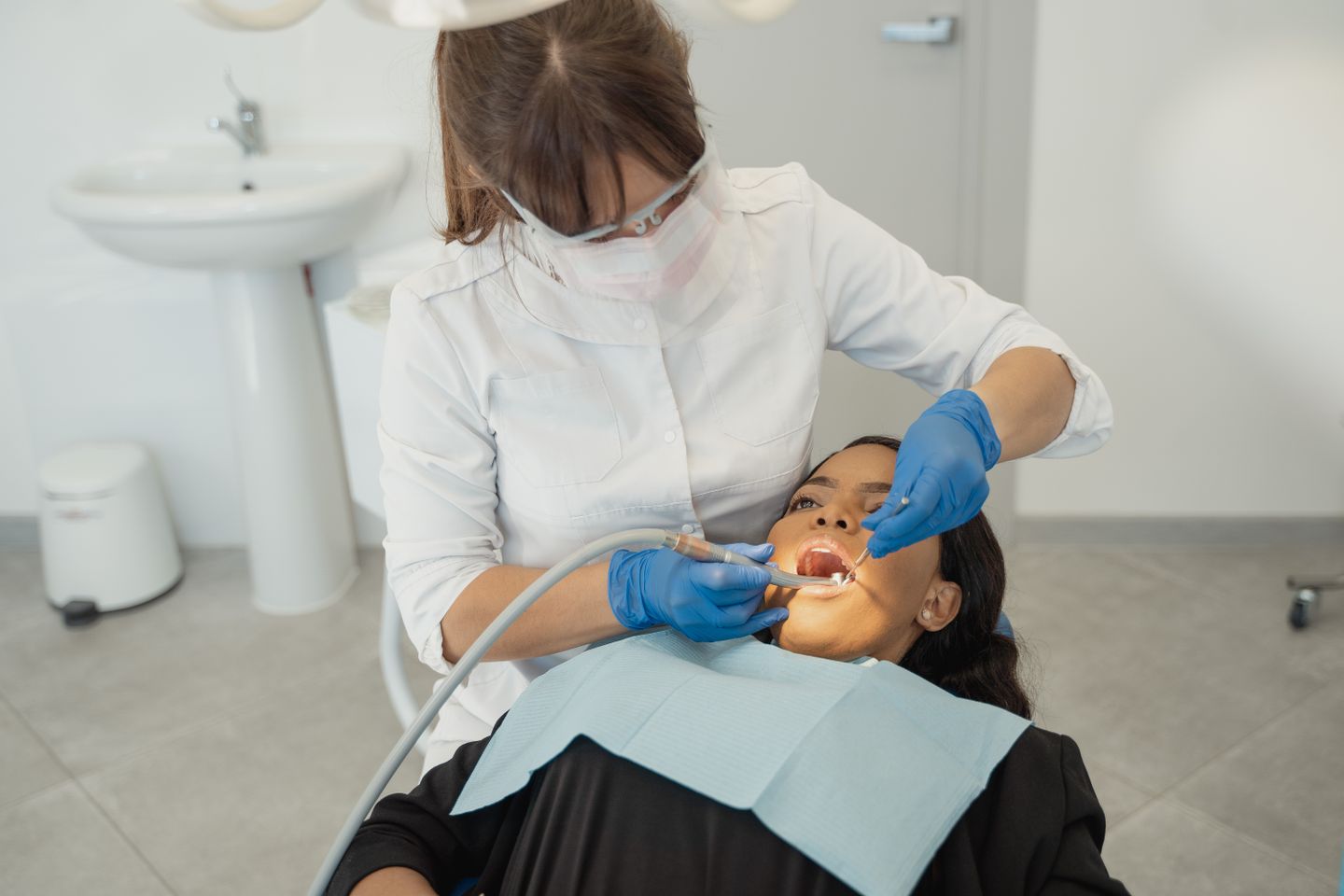 A dentist in a mask examining a patient's teeth in a clinic