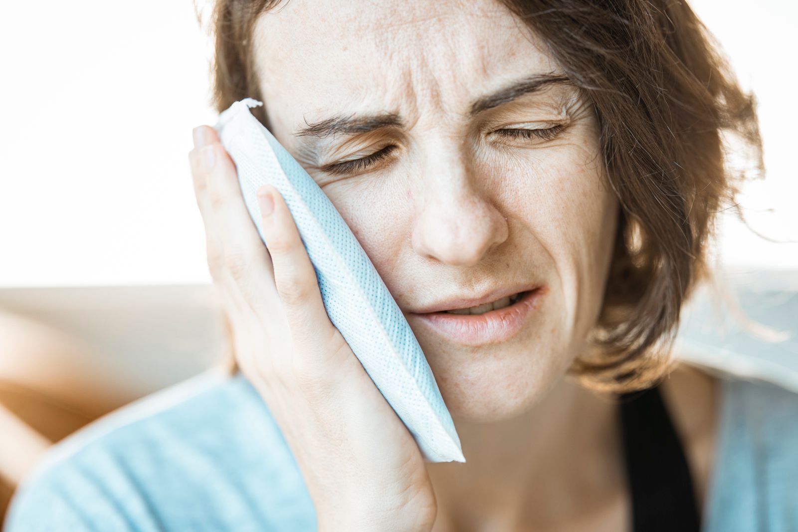 A woman holding a cold compress against her cheek to ease tooth pain