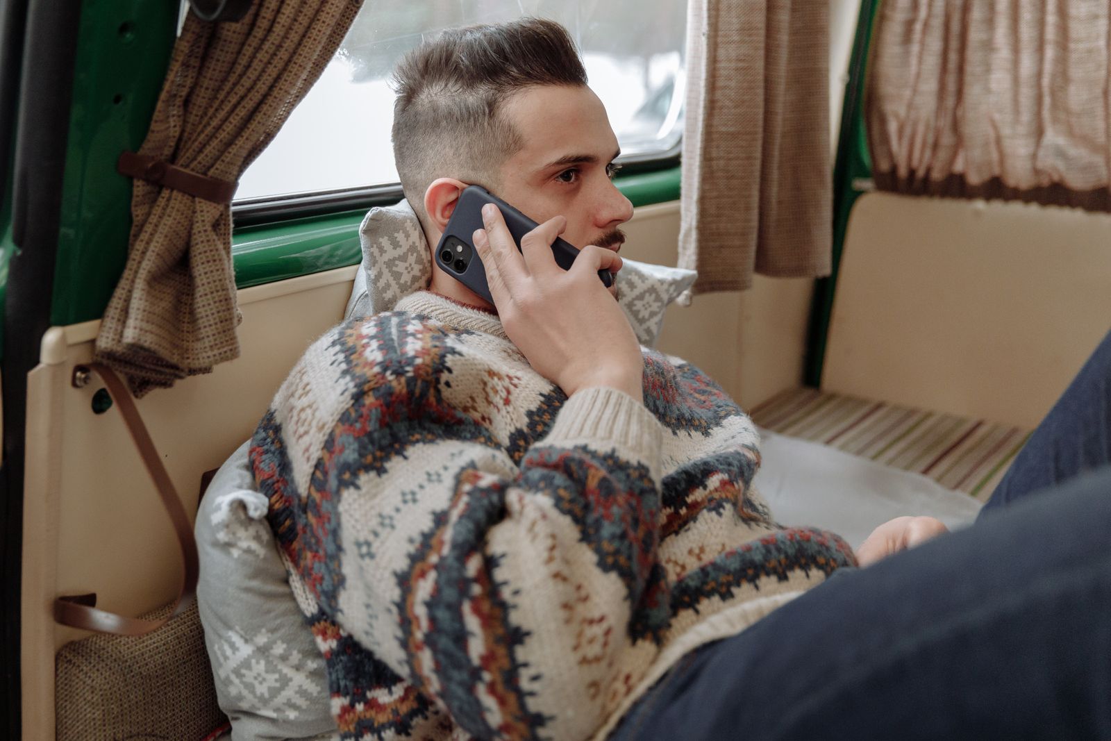 A man at home making a phone call, sitting calmly by a window