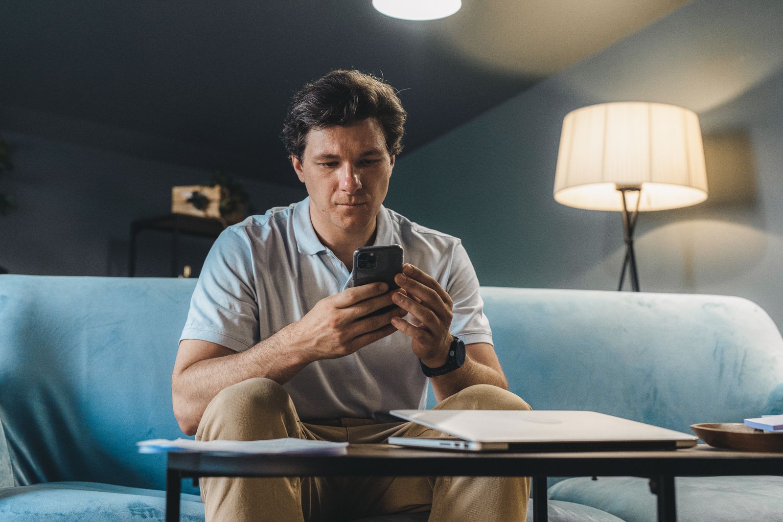 A man sitting on a sofa in a warmly lit room at night, making a phone call