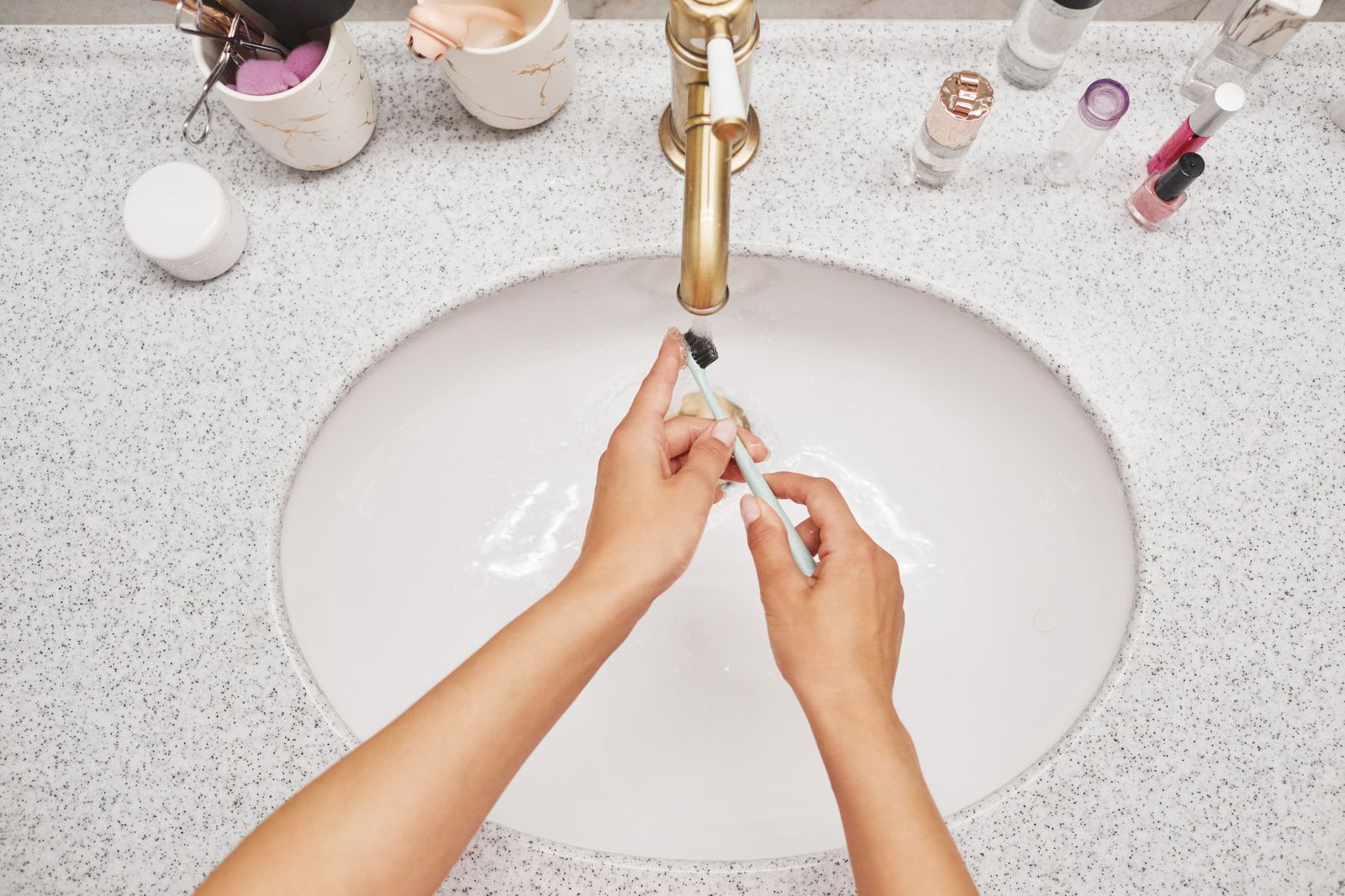 A toothbrush being rinsed under running water at a bathroom sink