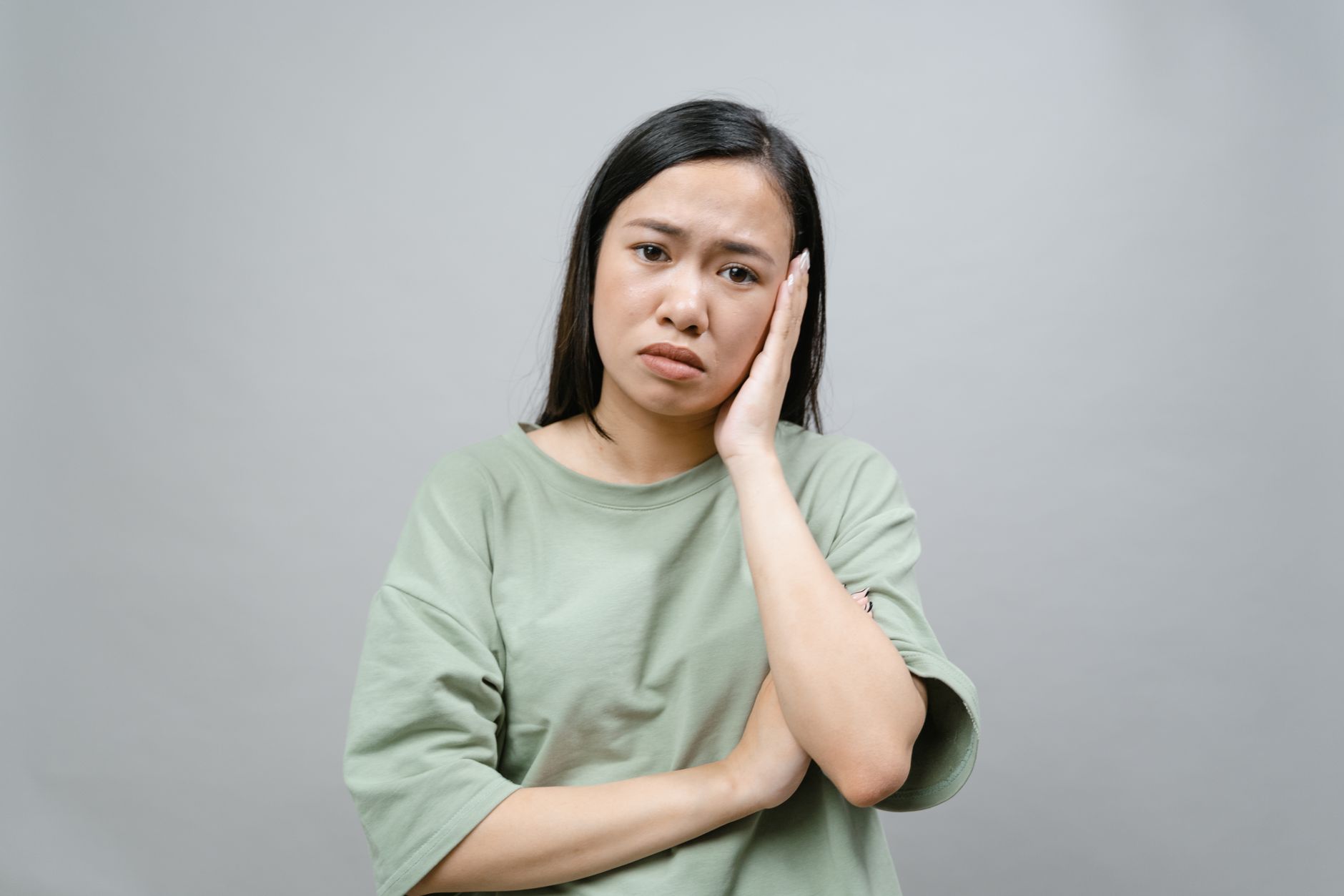 A woman with a concerned expression, worried about a tooth infection she has been ignoring for weeks