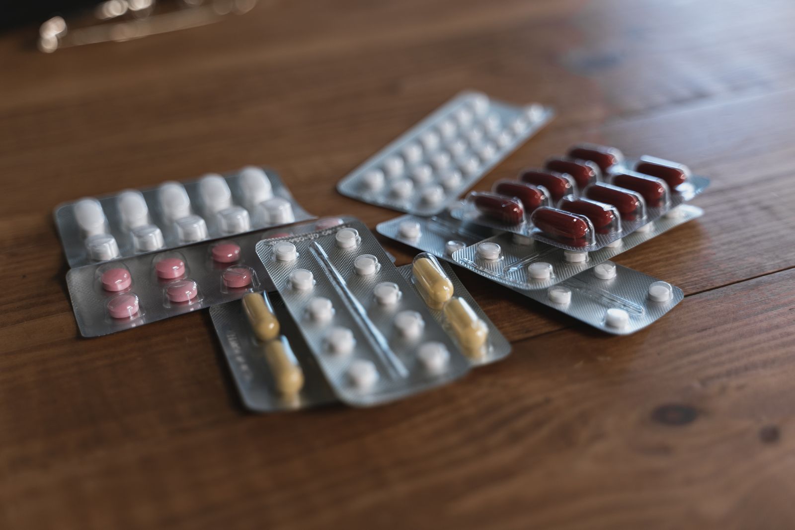 Assorted packs of over-the-counter pain relief tablets on a wooden table