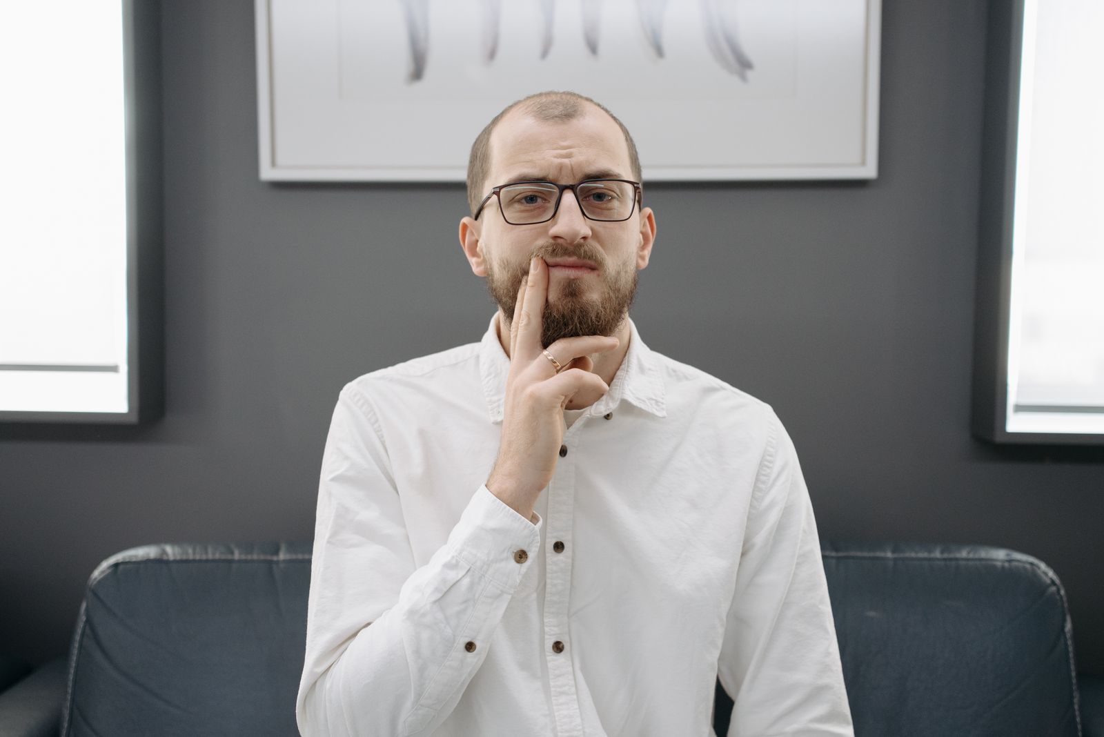 A man in glasses and a white shirt pressing his fingers against his cheeks, thinking about an aching tooth