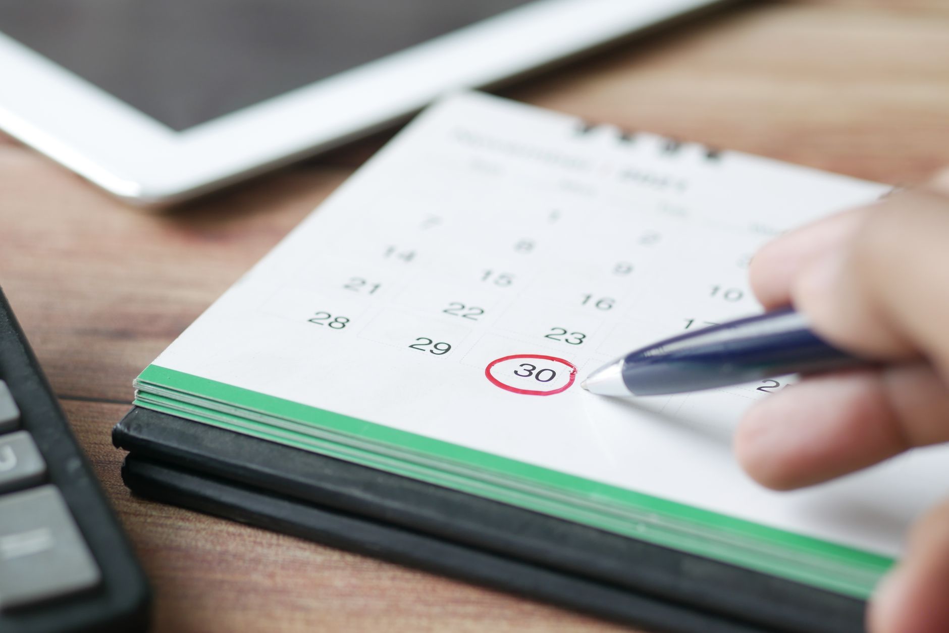 A hand marking a date on a wall calendar with a pen
