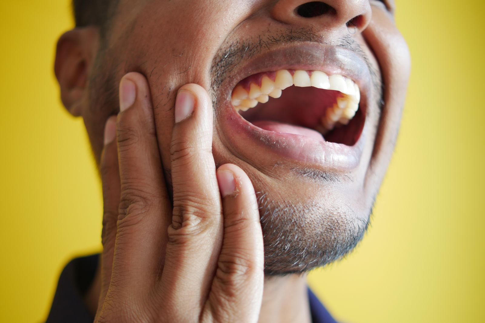 A man pressing his hand against his jaw with his mouth open in obvious pain