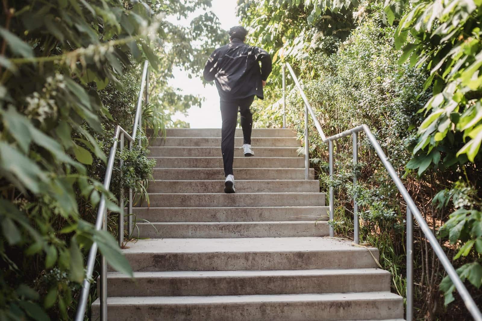 A man in sports clothes running up outdoor steps surrounded by greenery