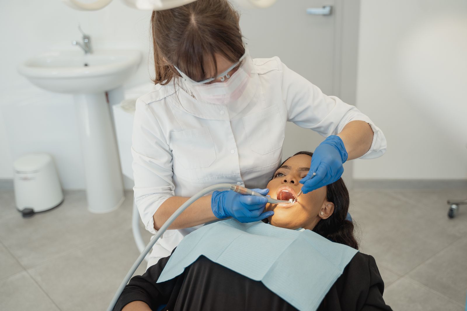 A dentist in a face mask examining a patient's teeth in a clinic