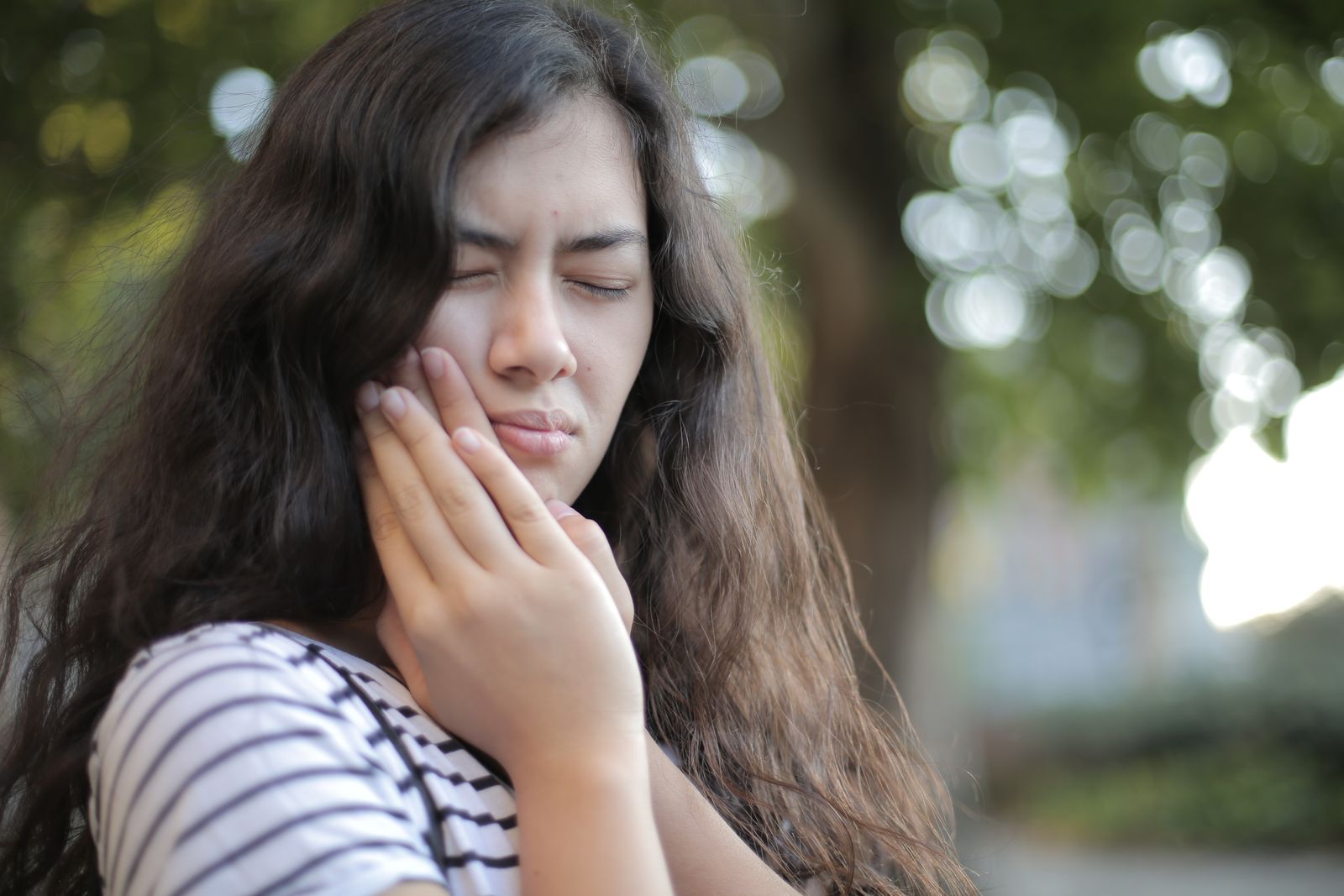 A young woman holding her cheek in discomfort from tooth pain