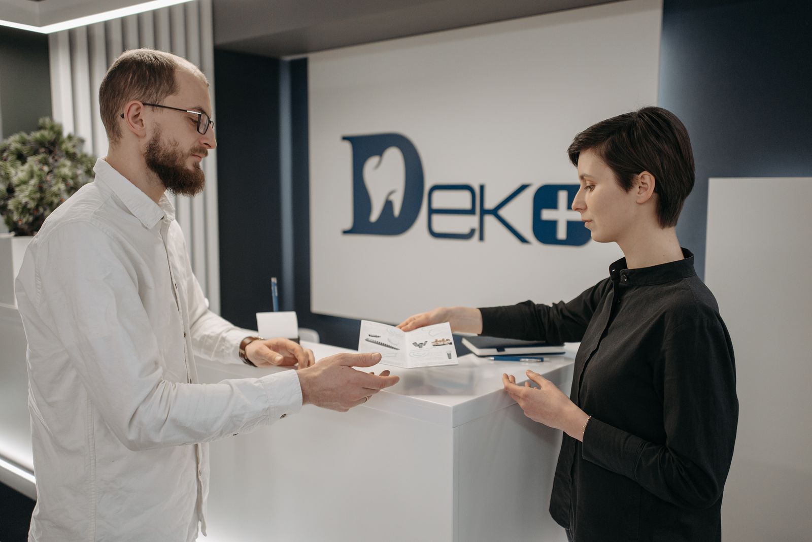 מטופל ופקידת קבלה מחליפים מסמכים בדלפק הקבלה של מרפאת שיניים