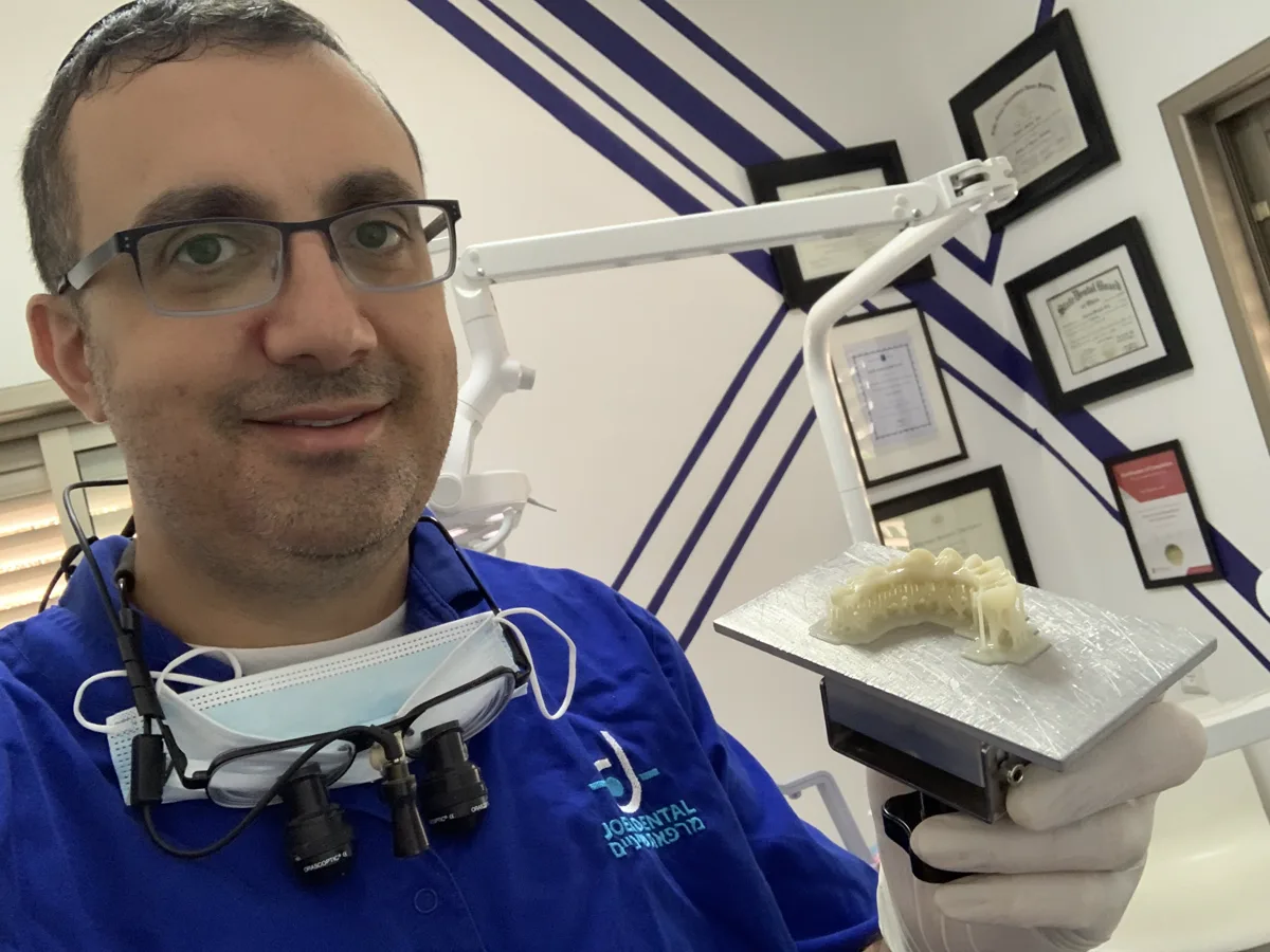 ד"ר גבריאל יואל עם משקפי הגדלה כירורגיים, מחזיק מודל שיניים מודפס בתלת מימד.